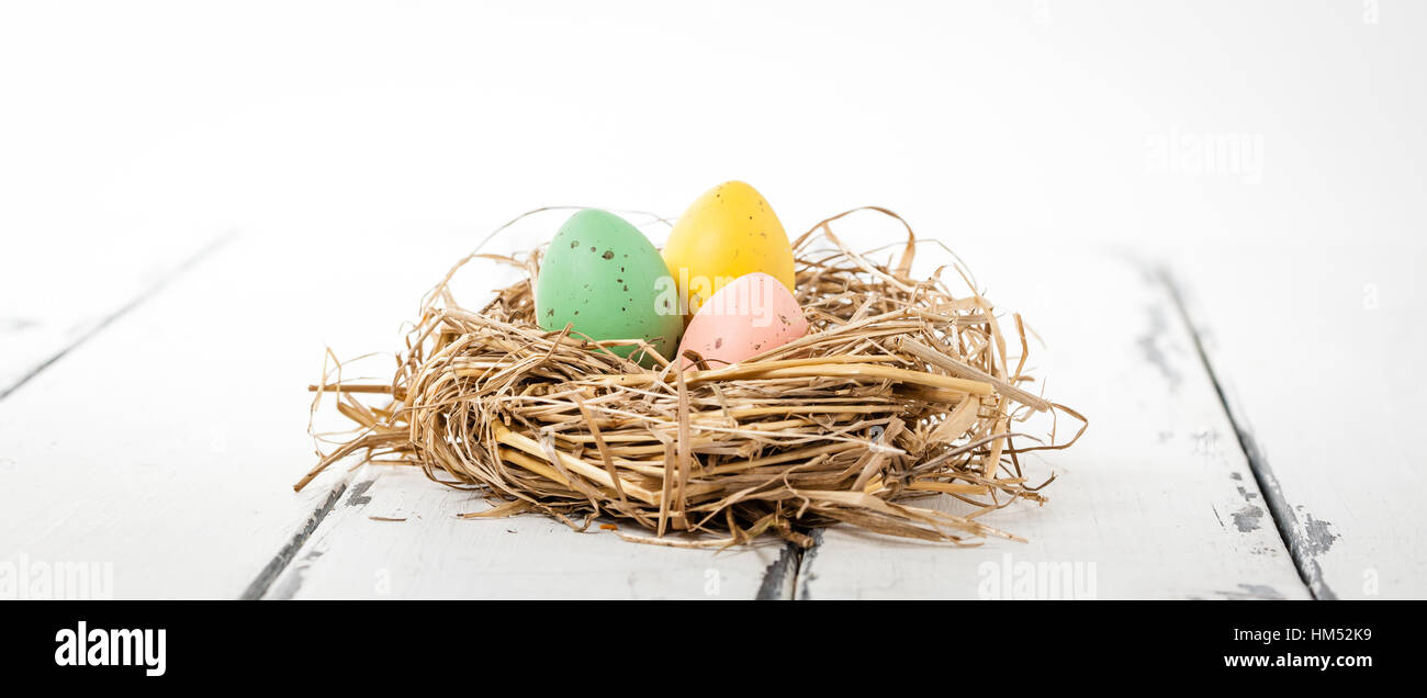 three ester eggs in a bird nest on white wooden background Stock Photo