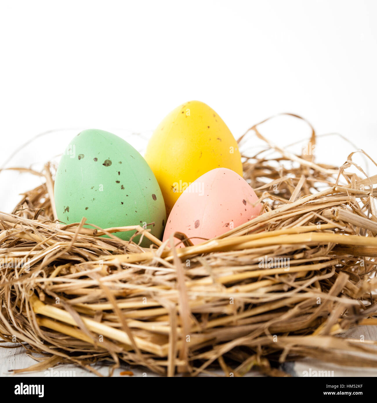 close up of three pastell colored eggs in a hay nest Stock Photo