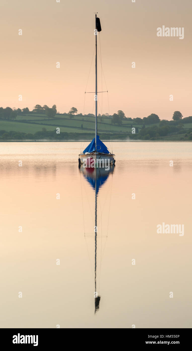 A small yacht perfectly reflected in the still water at sunset. Stock Photo
