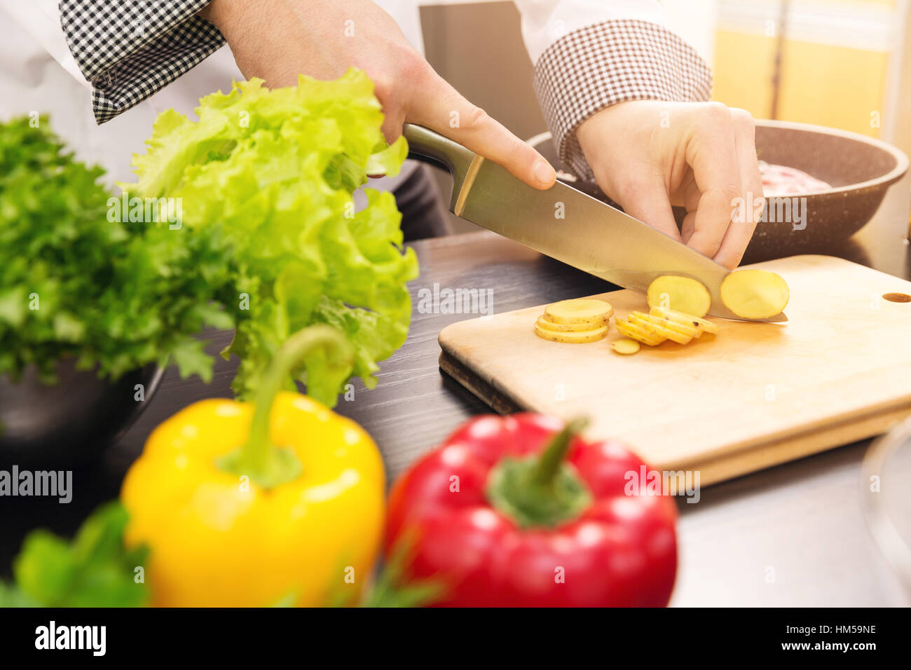 chef slicing potato on wooden board in kitchen Stock Photo