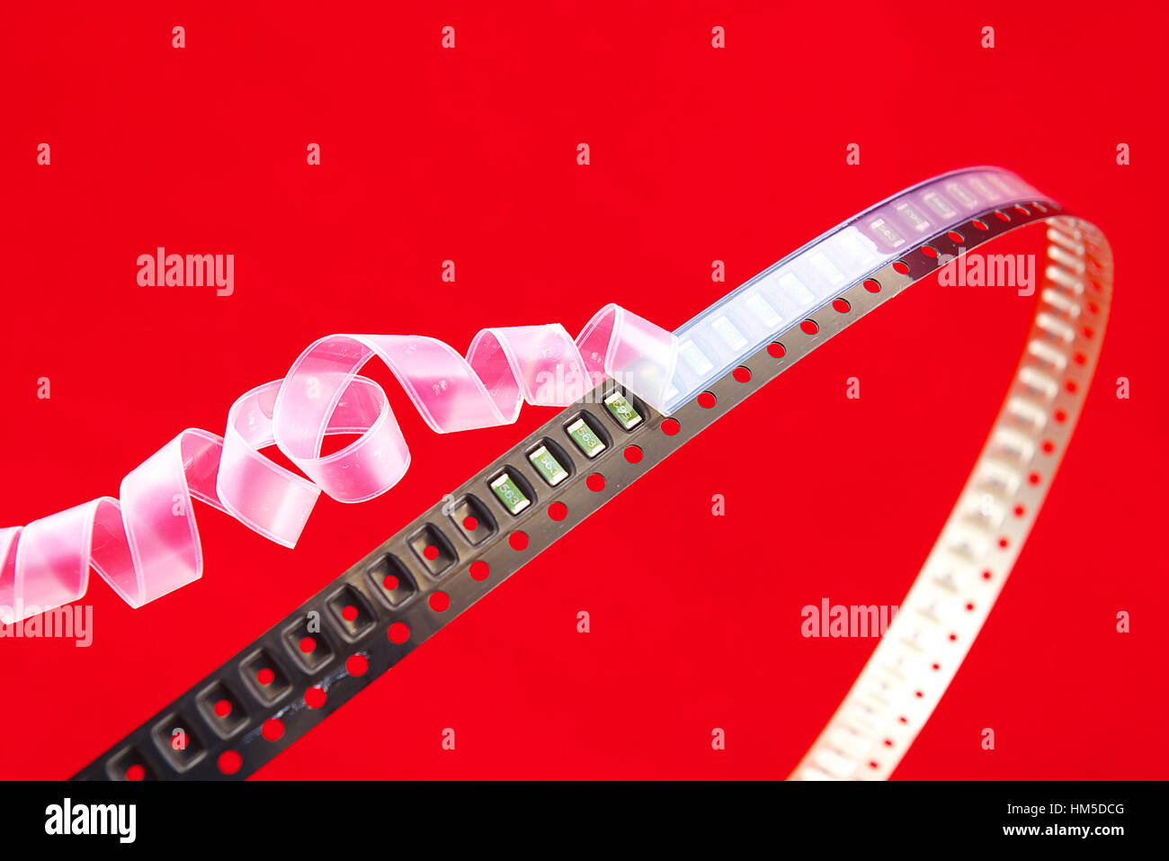 SMD components on a black plastic carrier tape with red background. White cover tape opens Christmas ribbon style. Stock Photo