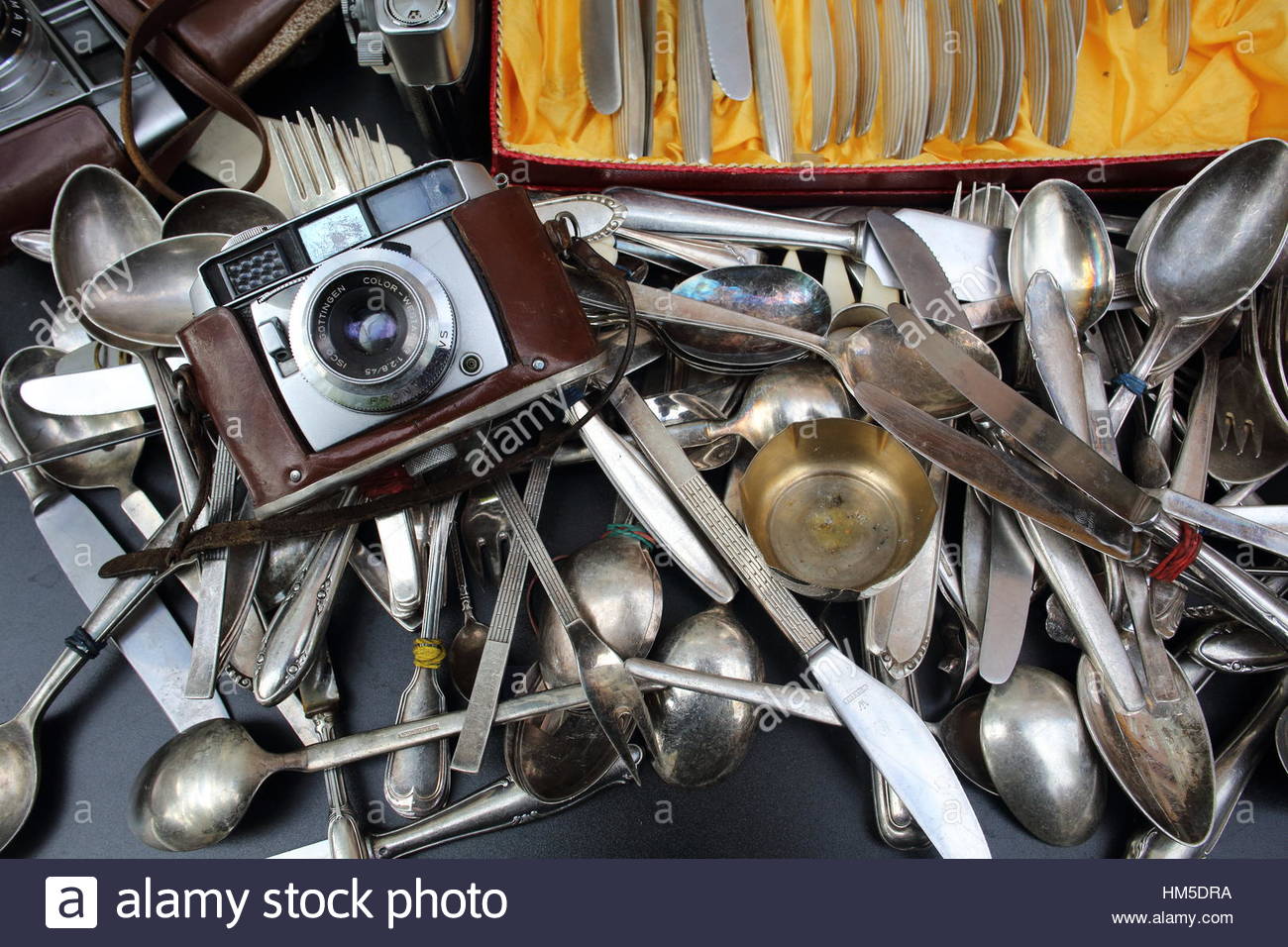 A camera and old silver spoons and knives all flung together in a second hand shop Stock Photo