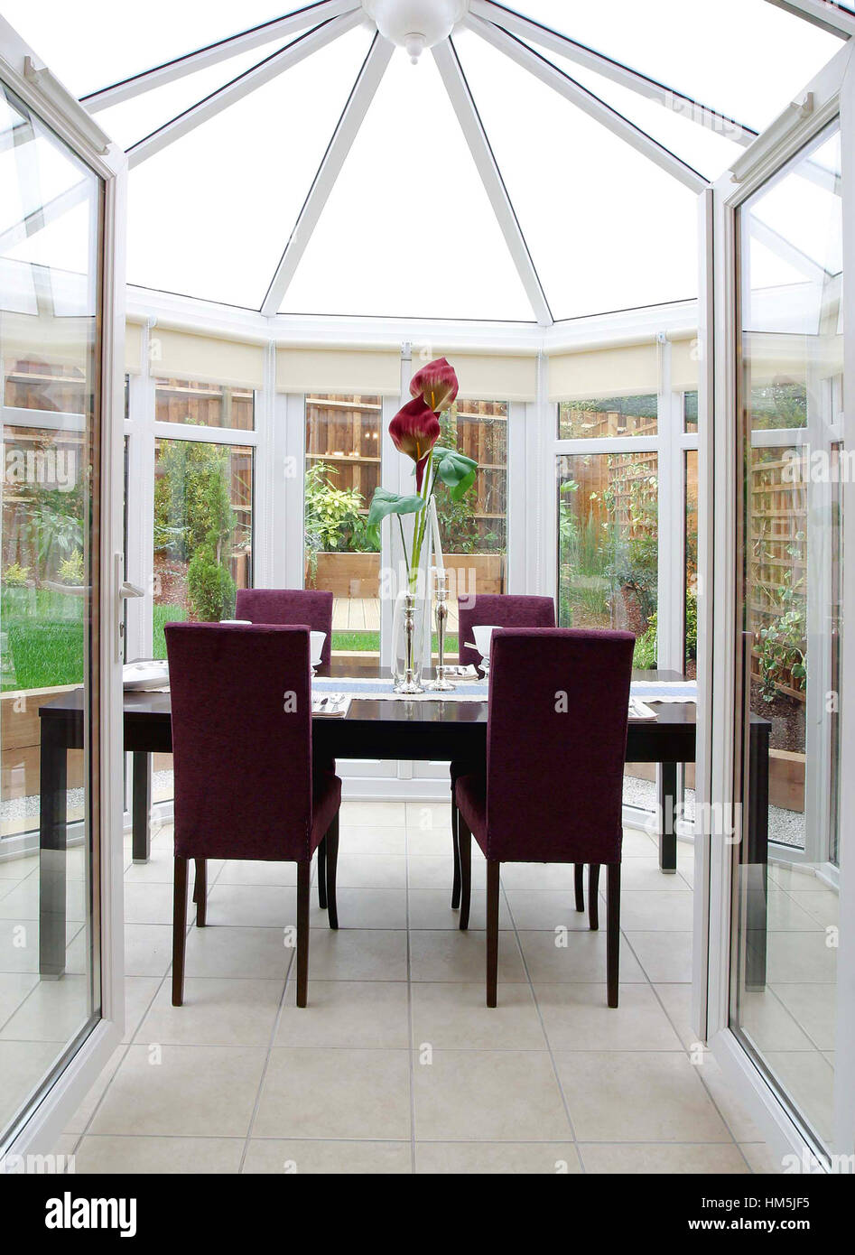 View into a conservatory laid as a dining room, red chairs, modern interior, lillies on the table, upright (portrait) orientation. Stock Photo