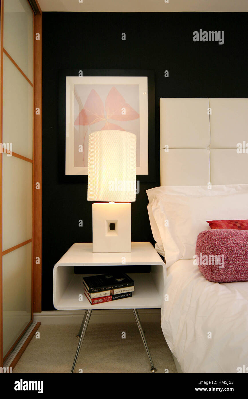 Modern bedside table on chrome legs beside bed and wardrobes Stock