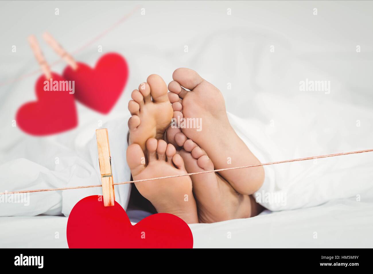 Composite image of red hanging hearts and couple lying on bed Stock Photo