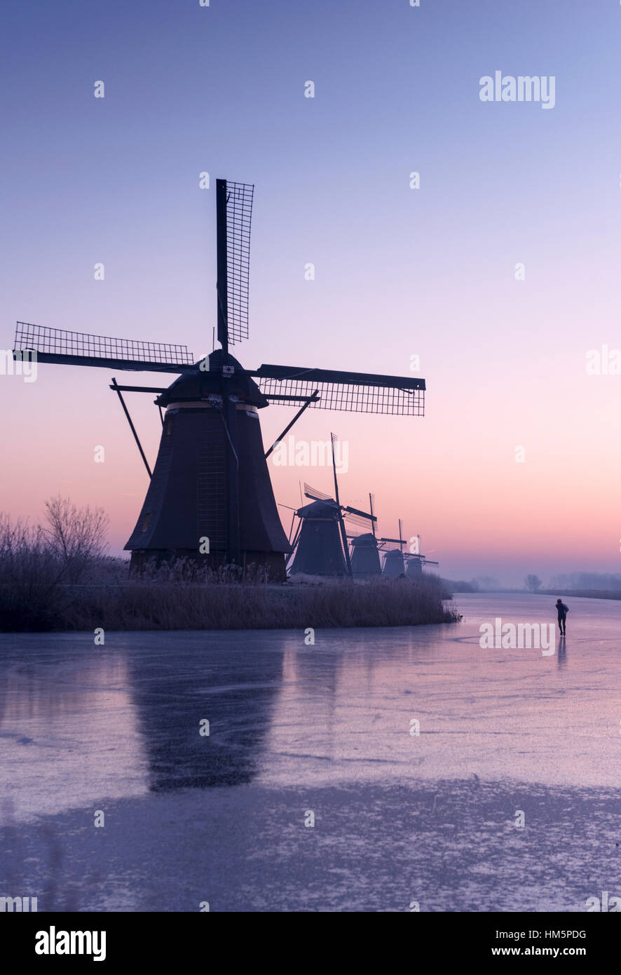 Winter sunrise over windmills at the Kinderdijk UNESCO World Heritage Site in the Netherlands, with someone skating on the ice Stock Photo