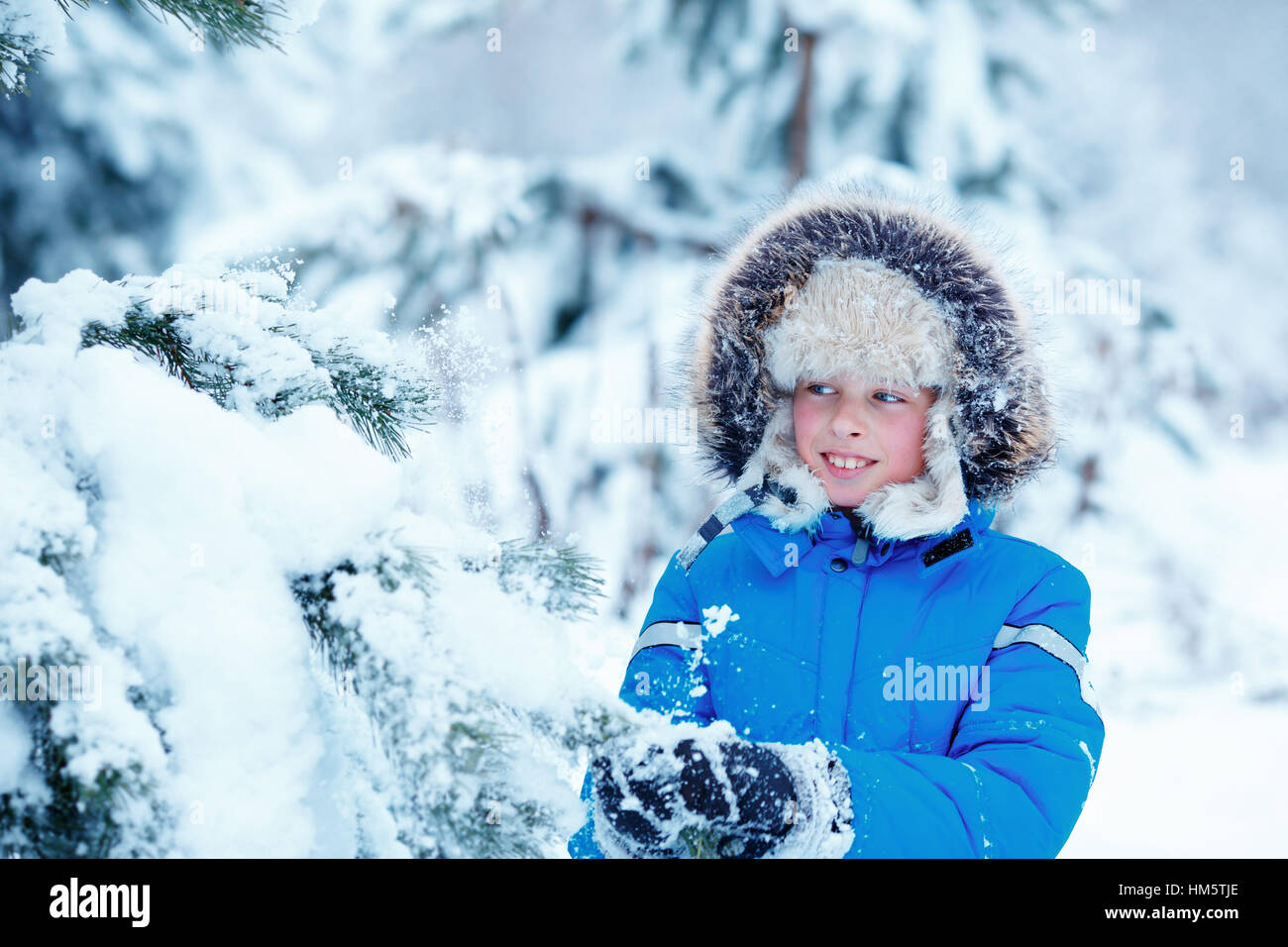 Cute little boy wearing warm clothes playing on winter forest Stock Photo