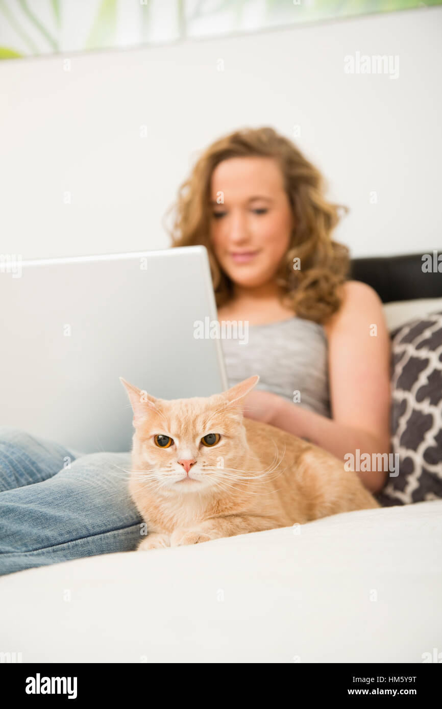Teenage girl (1617) lying on bed with laptop and ginger tabby cat