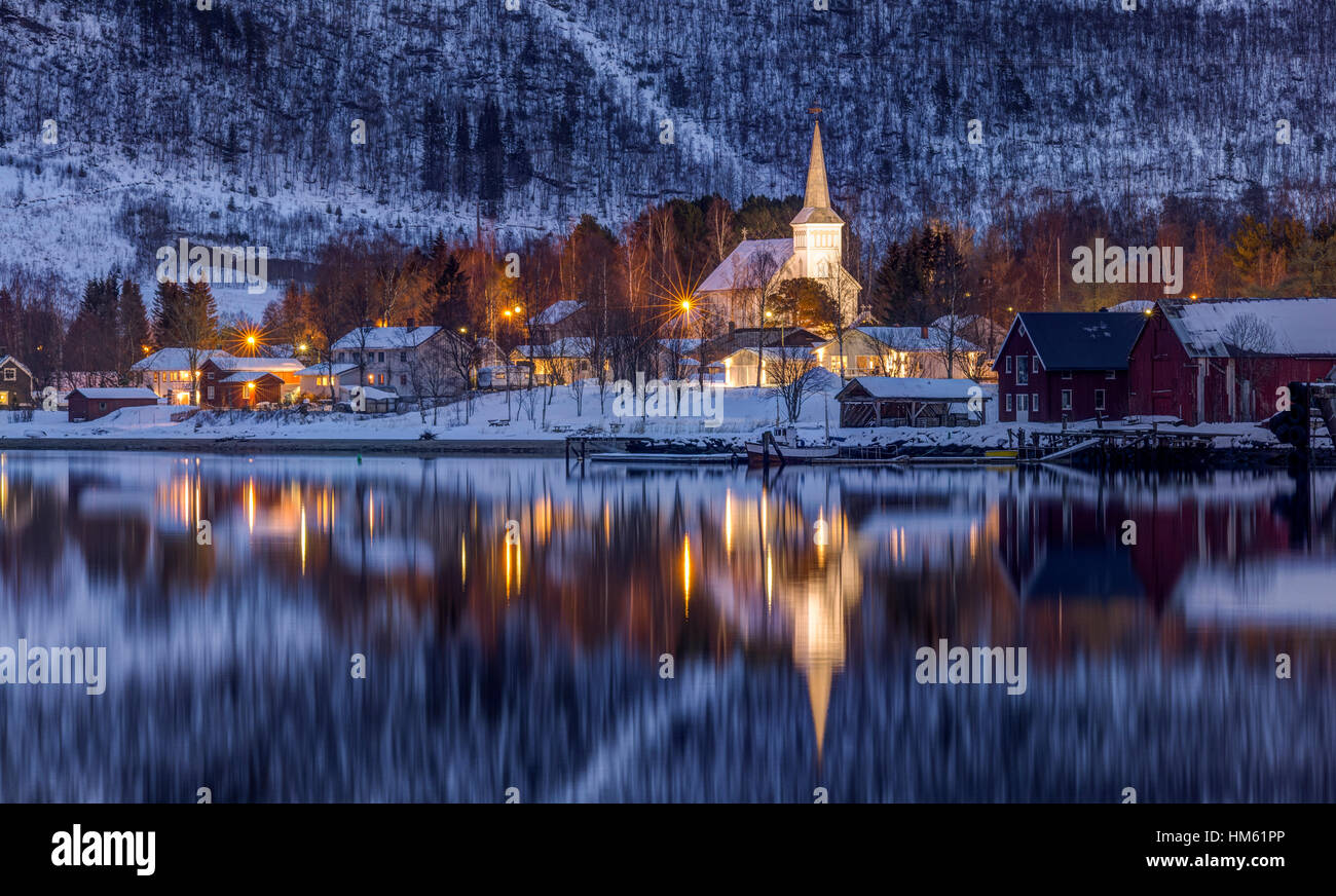 Evening in the small town of Rognan in Northern Norway, above the Arctic Circle. On the shores of the fjord is an illuminated protestant church. Stock Photo