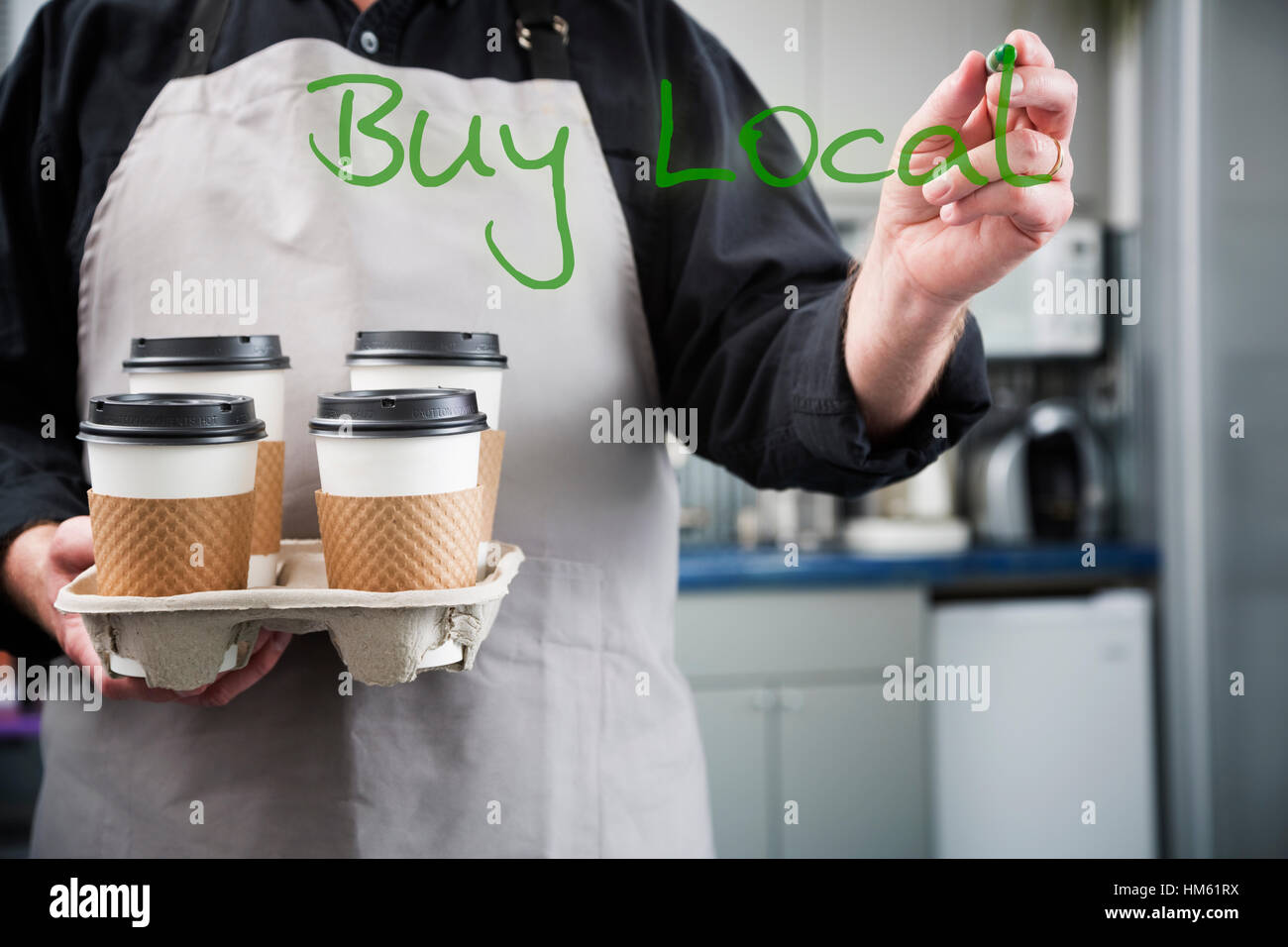 Man holding four cups of coffee and writing 'buy local' on glass using sharpie Stock Photo