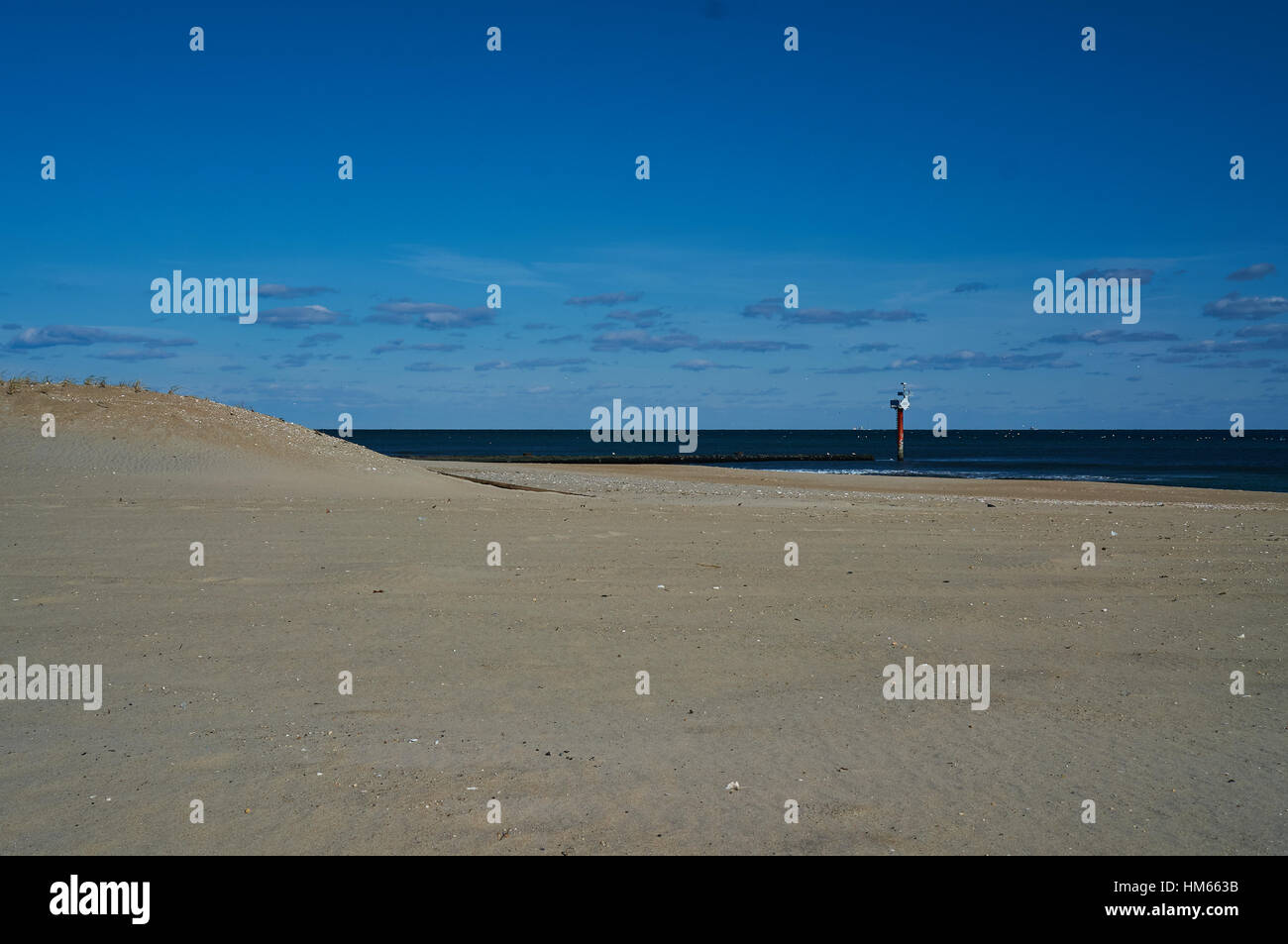 portion of beach, rocky jetty, and coastline marker with ocean horizon and blue sky and clouds Stock Photo
