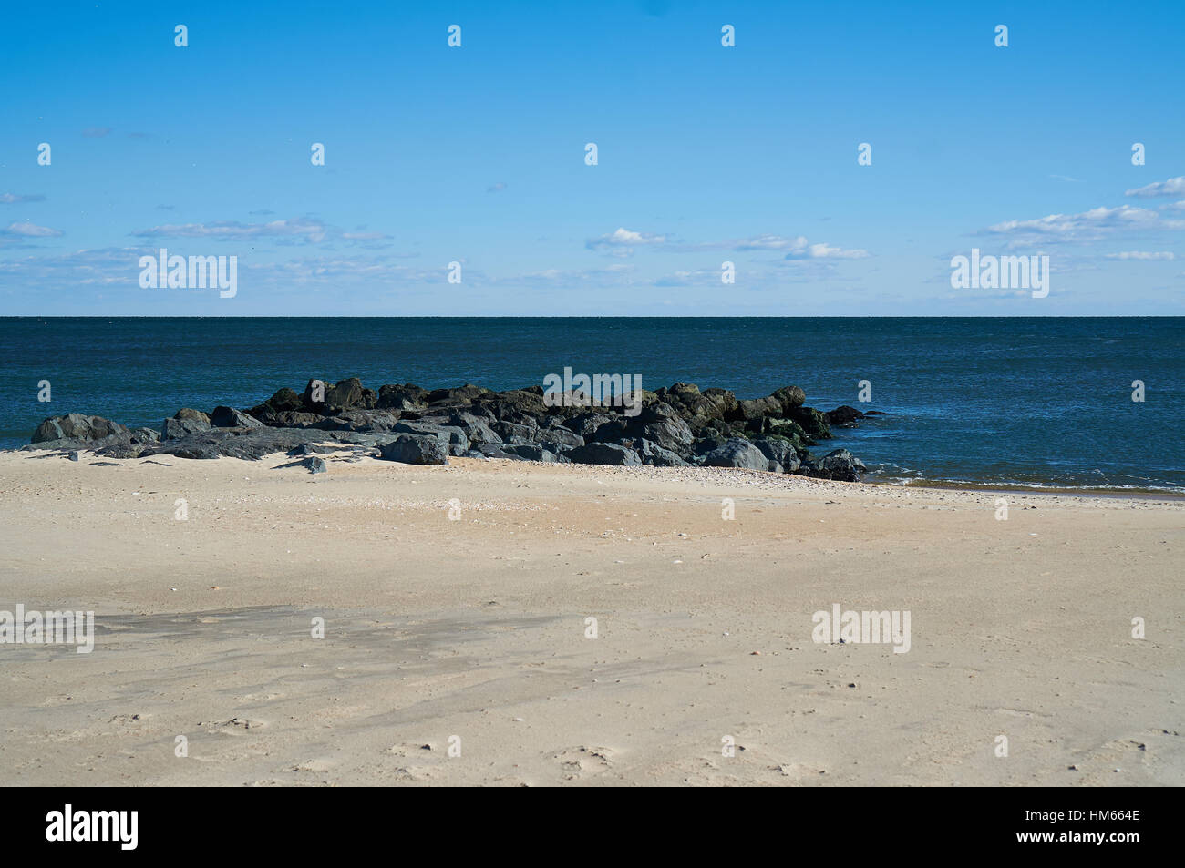 coastline including beach and rocky jetty with ocean horizon and blue sky and clouds Stock Photo