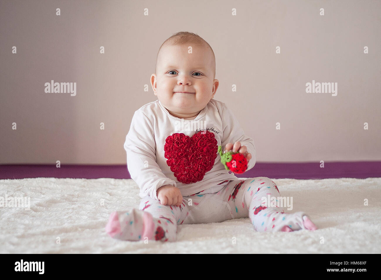 Smiling baby girl with heart on her t-shirt and strawberry in her hands. White bright background. Stock Photo