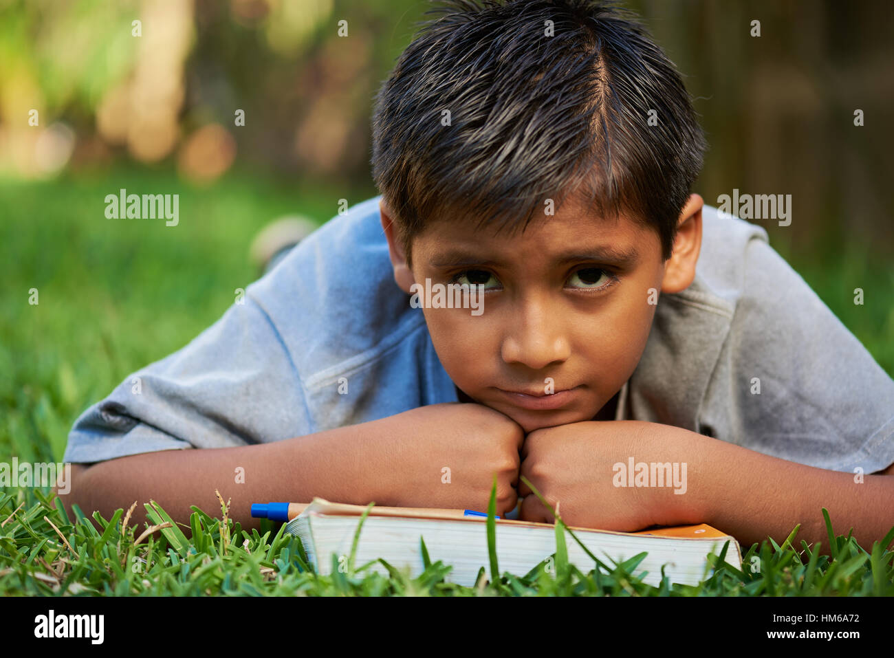 sad boy with book lay on green grass Stock Photo