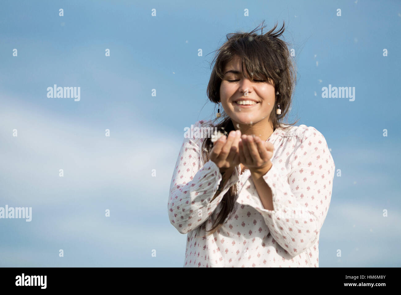 junge Frau hält Samen der Pusteblume in den Händen, die vom Wind verweht werden Stock Photo