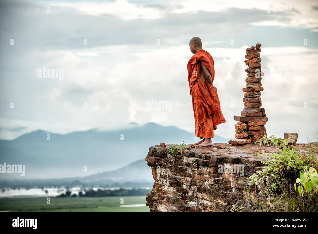 MINGUN, Myanmar - A Buddhist monk gazes out over the view of the Ayeyarwaddy River from the top of the Unfinished Pagoda in Mingun. Mingun Pahtodawgyi, also known as the Unfinished Pagoda of Mingun, was commissioned by King Bodawpaya in 1790. The current structure stands 50 meters tall; the plans called for it to reach a total height of 150 meters when completed. The structure is solid and built entirely of bricks. An earthquaker in March 1839 tore large cracks in the structure. Stock Photo