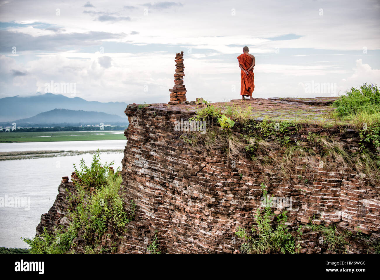 MINGUN, Myanmar - A Buddhist monk gazes out over the view of the Ayeyarwaddy River from the top of the Unfinished Pagoda in Mingun. Mingun Pahtodawgyi, also known as the Unfinished Pagoda of Mingun, was commissioned by King Bodawpaya in 1790. The current structure stands 50 meters tall; the plans called for it to reach a total height of 150 meters when completed. The structure is solid and built entirely of bricks. An earthquaker in March 1839 tore large cracks in the structure. Stock Photo