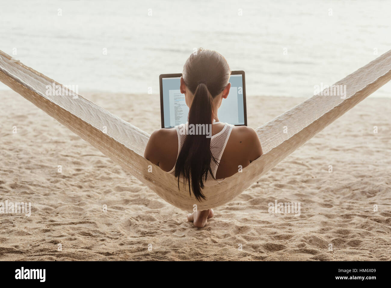 Rear view of woman using laptop computer while relaxing on hammock Stock Photo