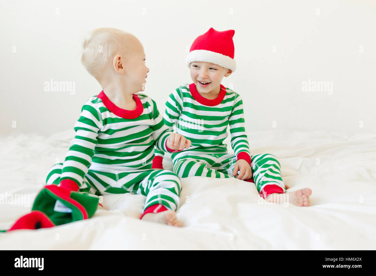 Siblings looking at each other while sitting on bed against white background Stock Photo