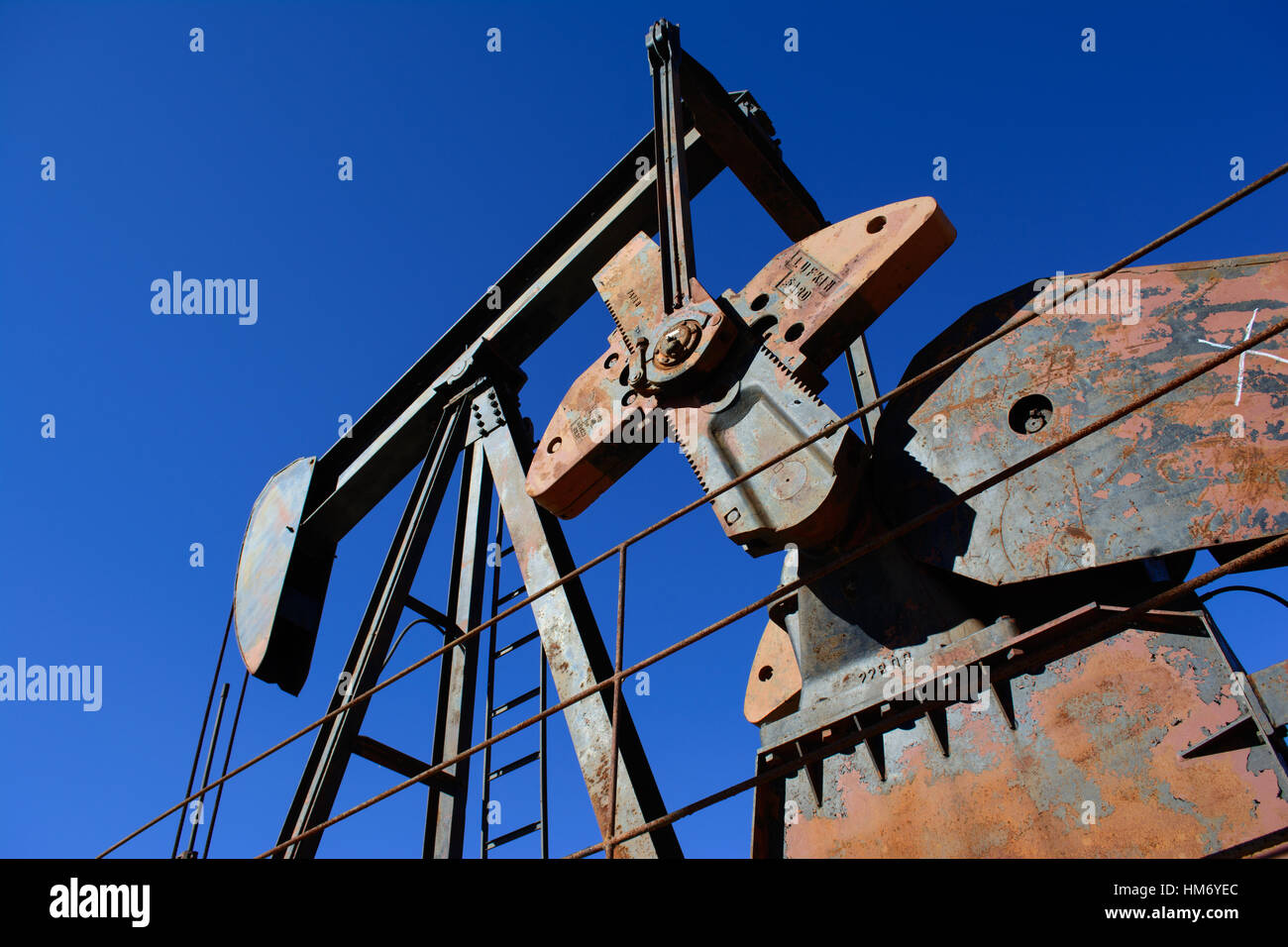 Rusty Oilfield Pumpjack (rocking horse) over a wellhead. Clear blue sky background. Illustrates oilfield life, petroleum industry and fossil fuels. Stock Photo