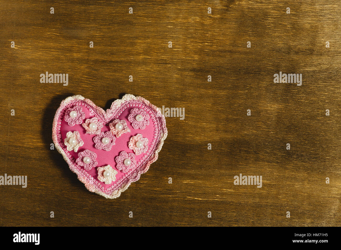 Pink heart of handwork with a pattern lies on a wooden background. A ...