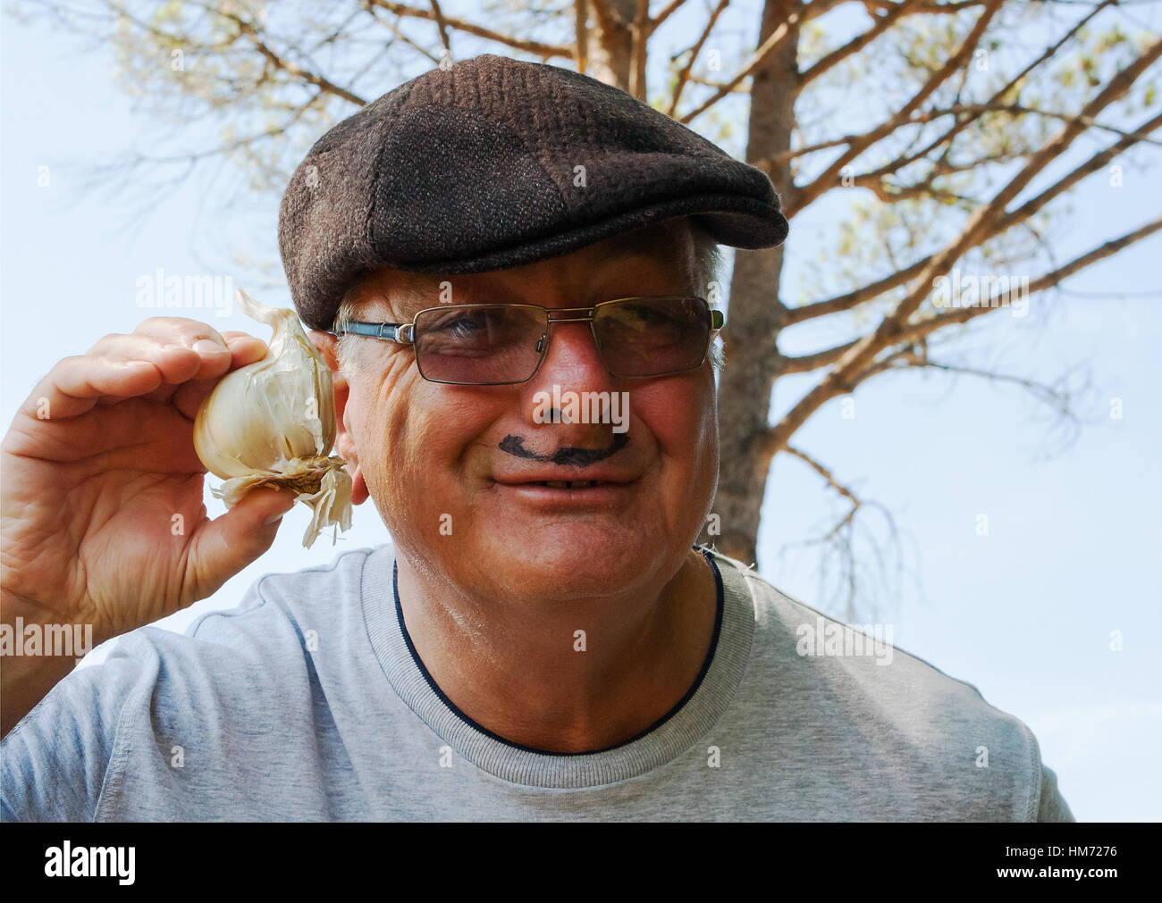 An elderly man mimicking a Frenchman with his cap, mustache, garlic and his own silly grin. Stock Photo