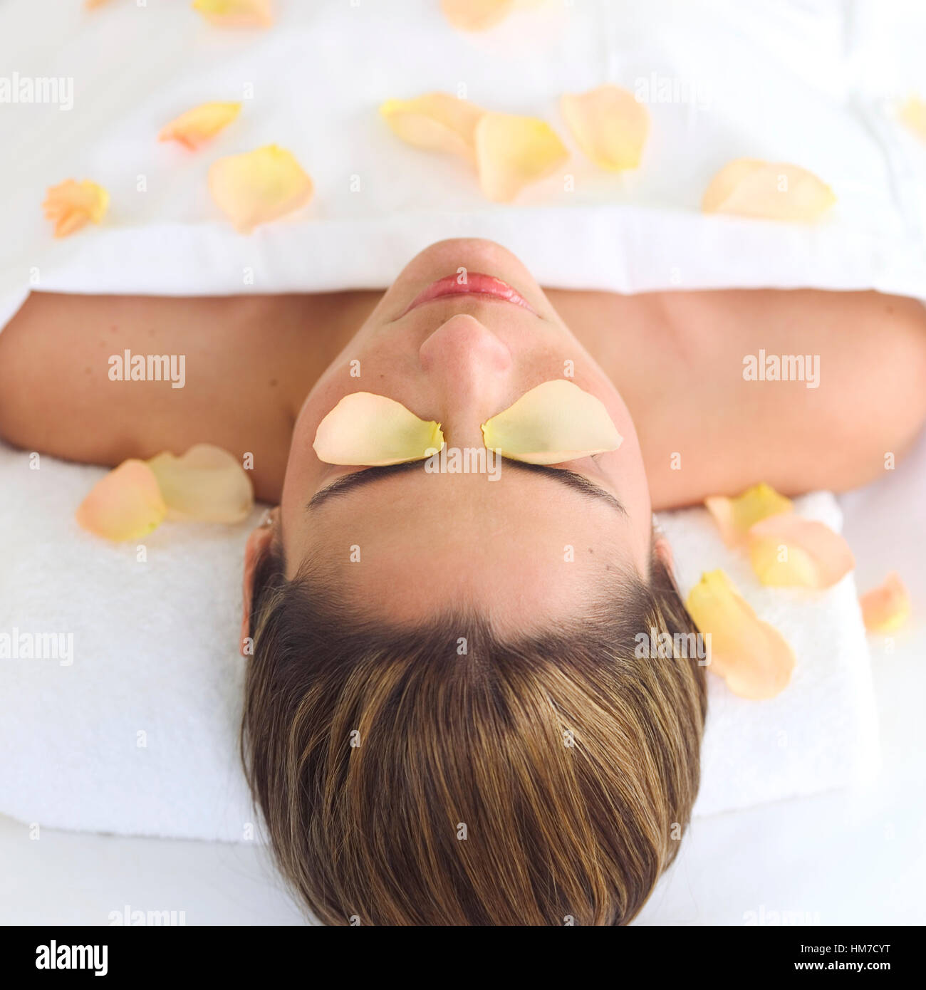 Mid adult woman lying on back under sheet covered with rose petals Stock Photo