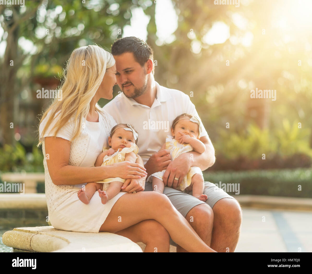 Happy family with two baby girls (2-5 months) at park in sunlight Stock Photo