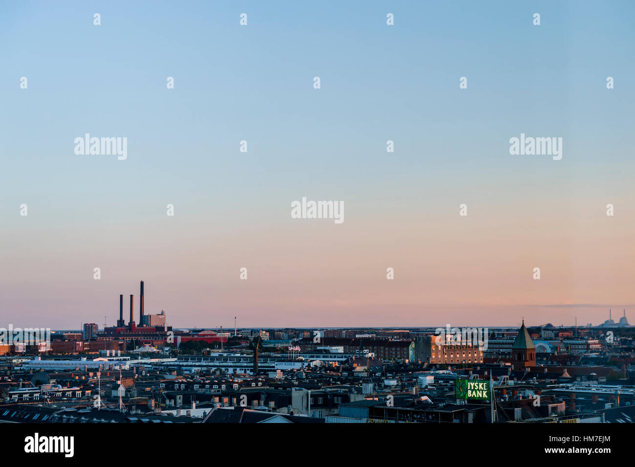 Factory chimneys rise above the flat city skyline of Copenhagen at sunset. Stock Photo