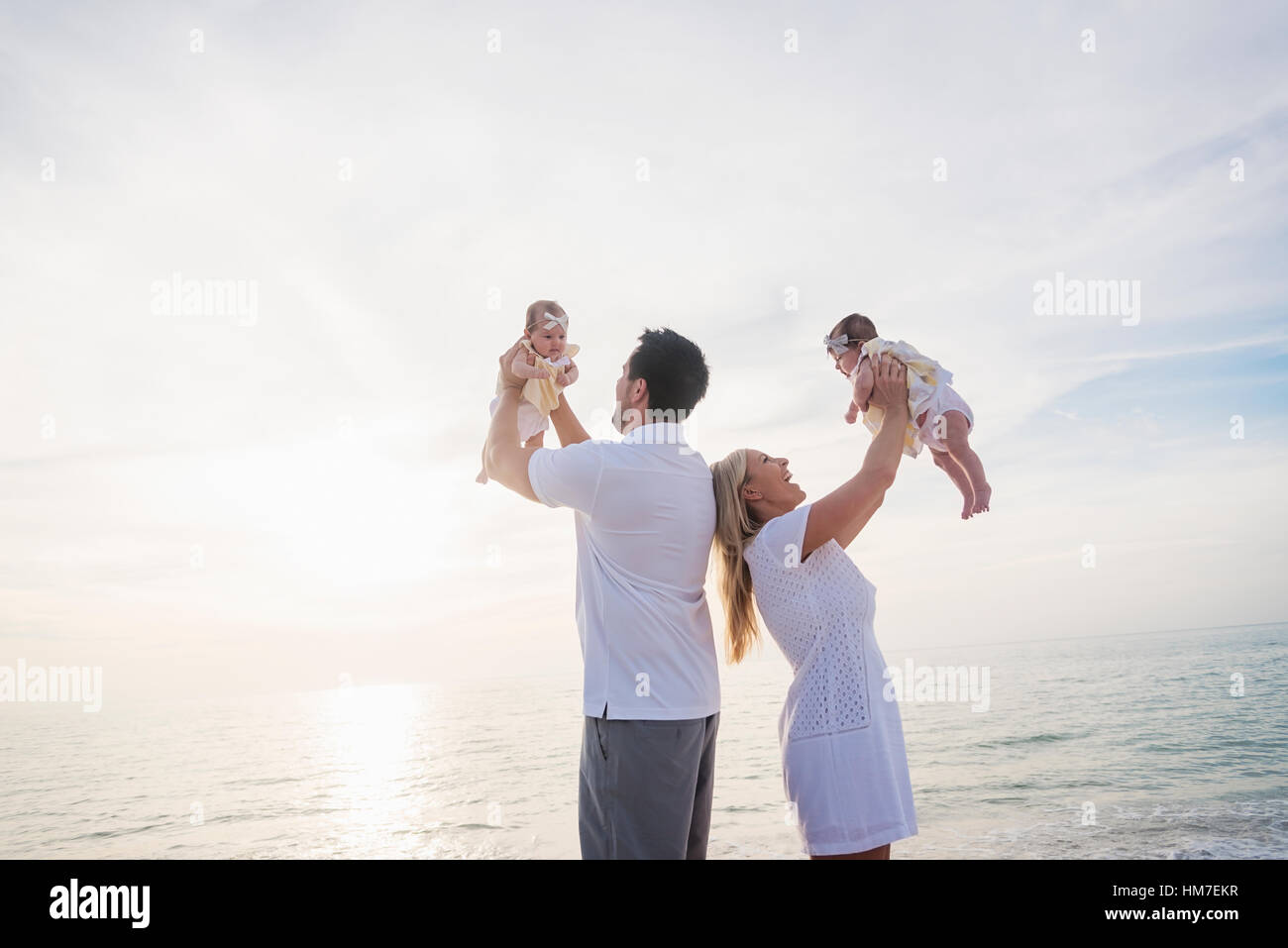 Happy family with two baby girls (2-5 months) at beach in sunlight Stock Photo