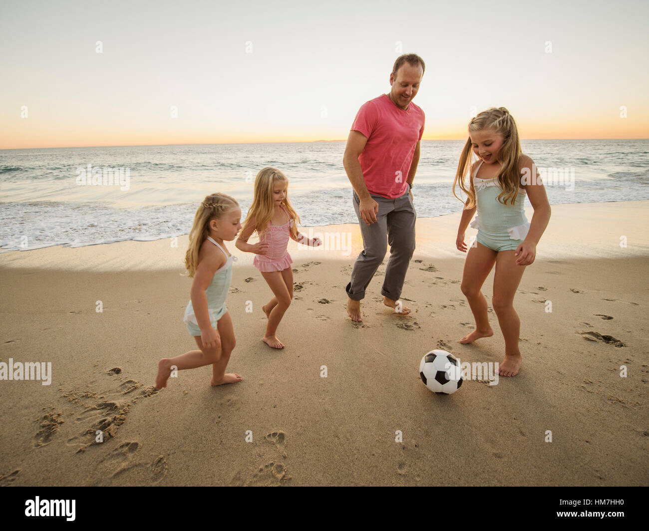 Father with children (4-5, 6-7, 8-9) playing soccer on beach Stock Photo