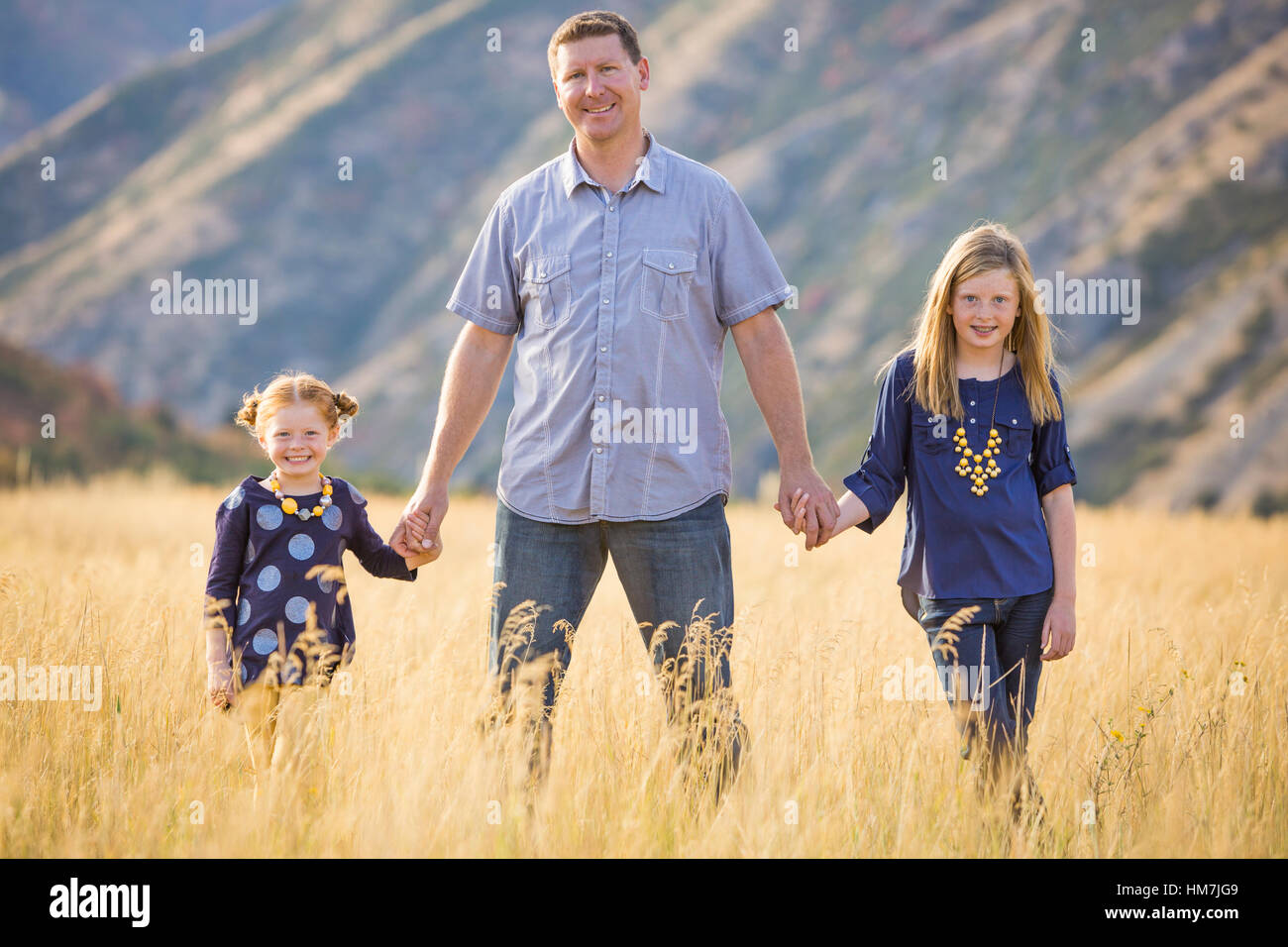 Father with two daughters (4-5, 8-9) walking in field Stock Photo
