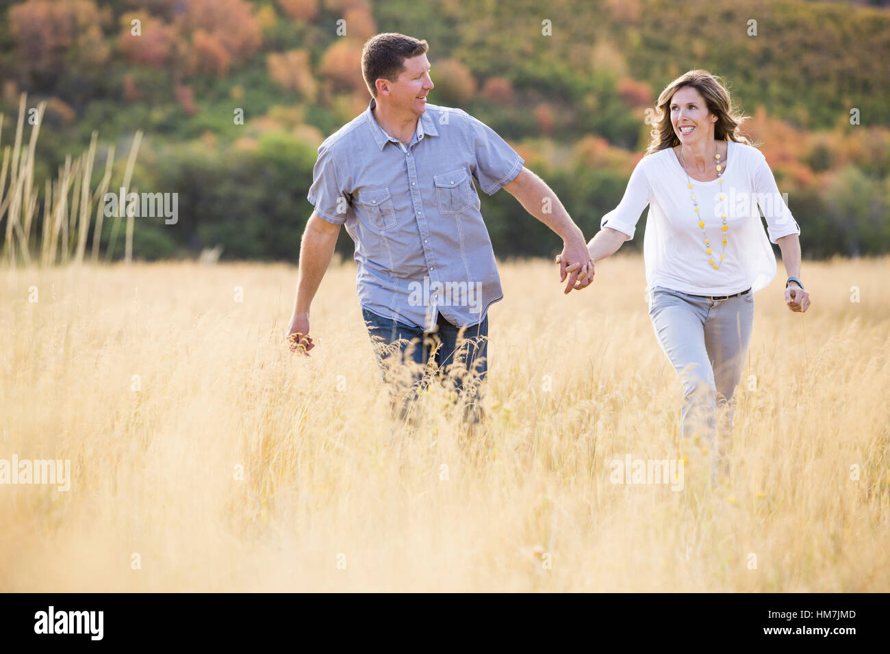 Smiling couple holding hands while walking in field Stock Photo - Alamy