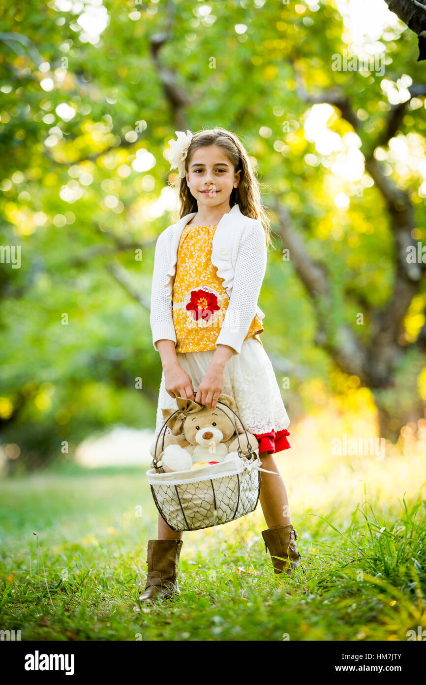 Smiling girl standing in orchard, holding basket with teddy bear Stock Photo