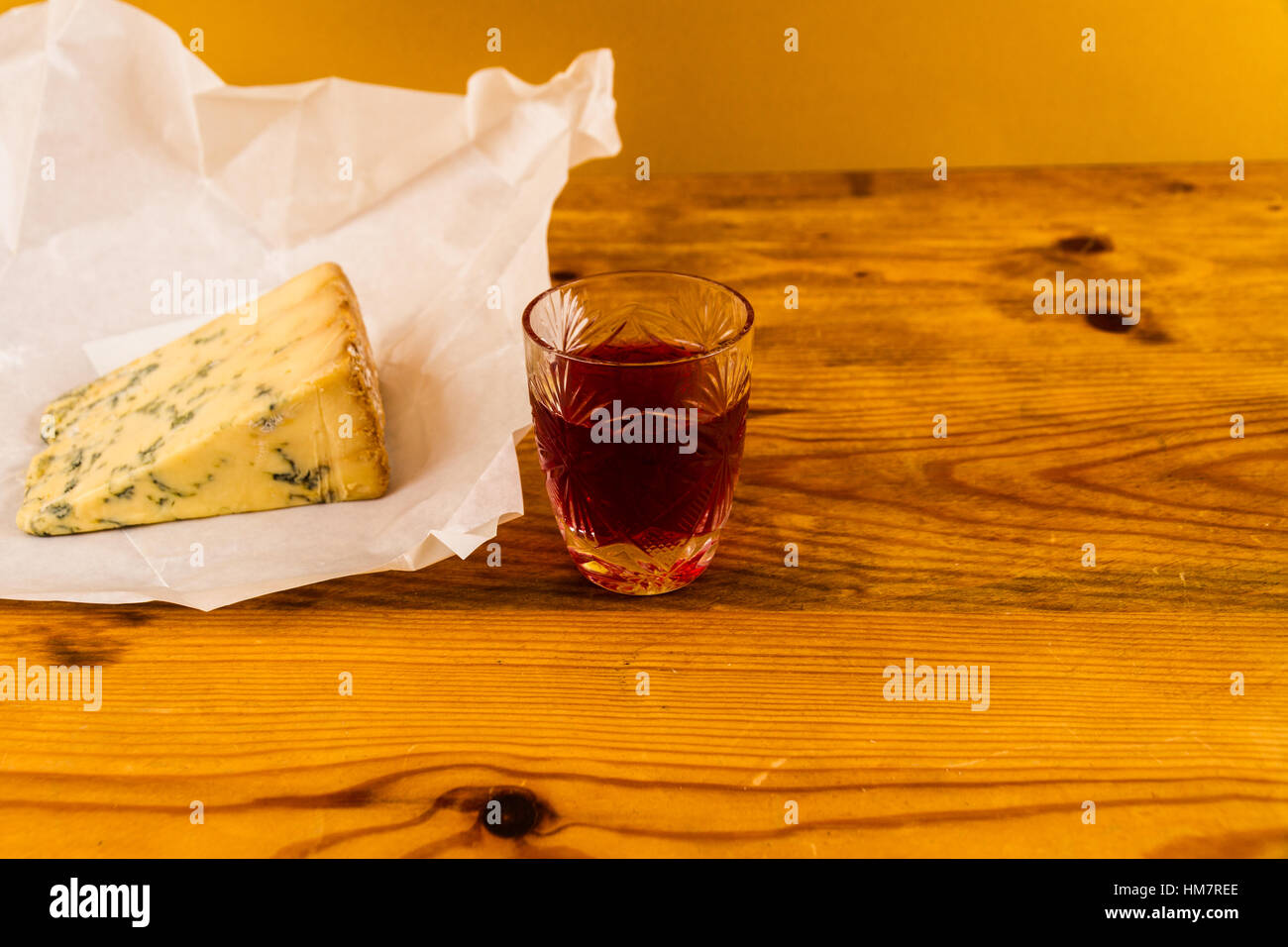 Shot glass with slow gin, beside a wedge of stilton cheese unwrapped greaseproof paper. Stock Photo