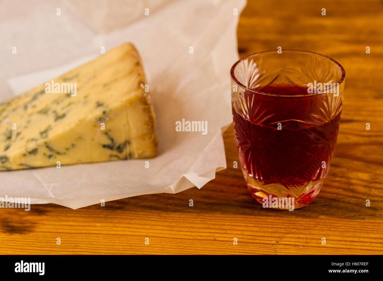Shot glass with slow gin, beside a wedge of stilton cheese unwrapped greaseproof paper. Stock Photo