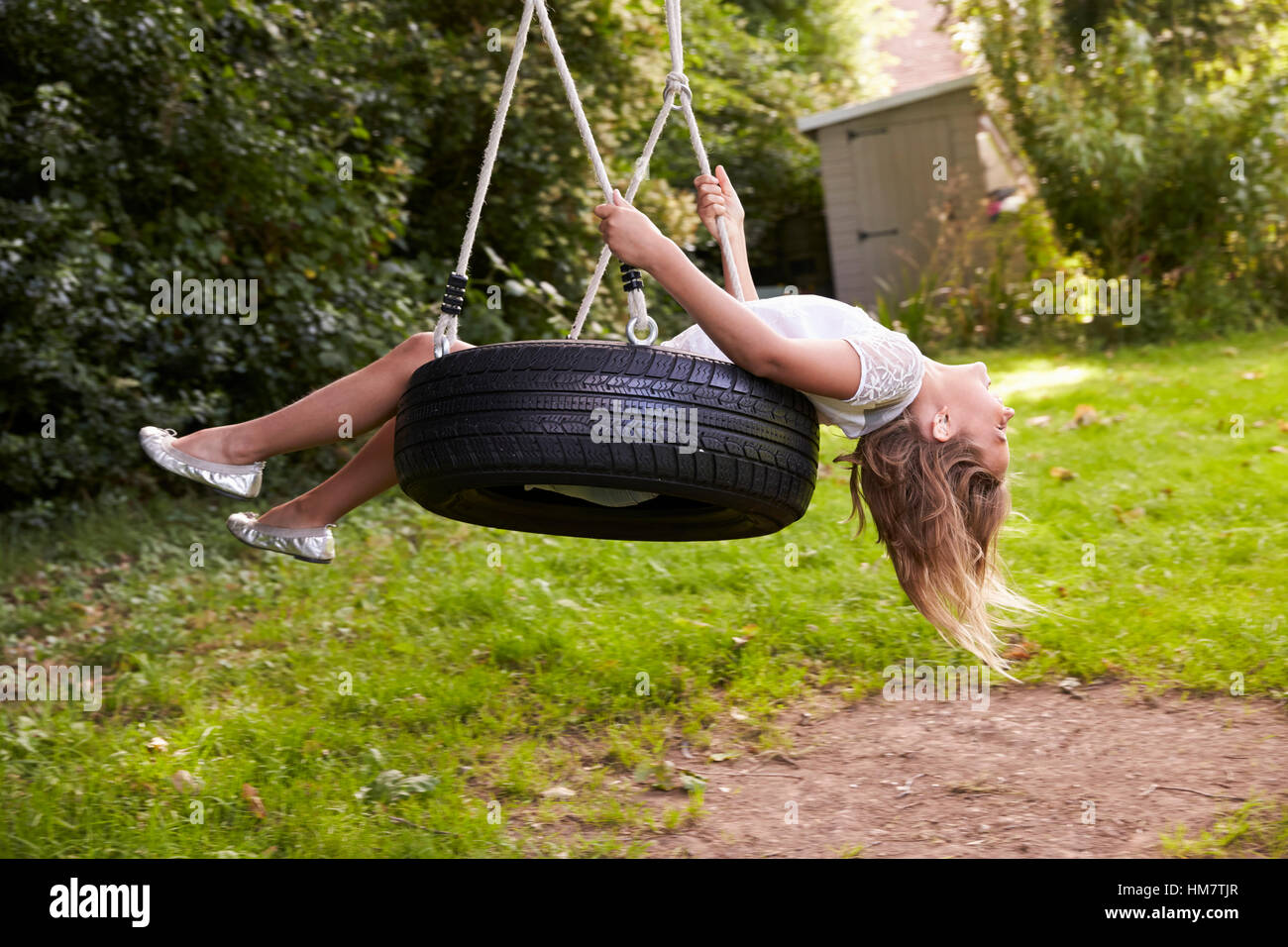 Young Girl Playing On Tire Swing In Garden Stock Photo