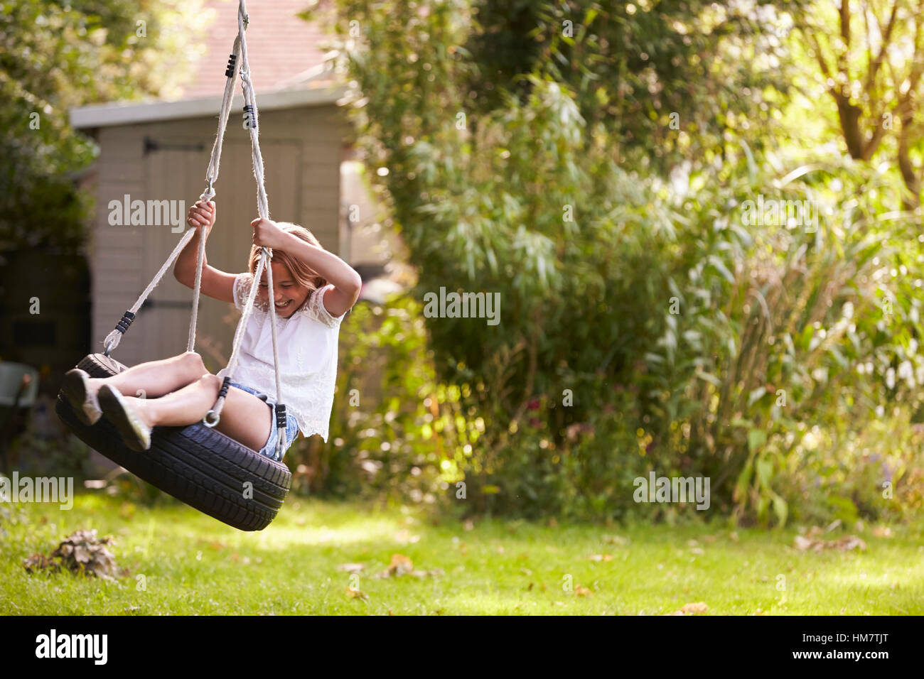 Young Girl Playing On Tire Swing In Garden Stock Photo