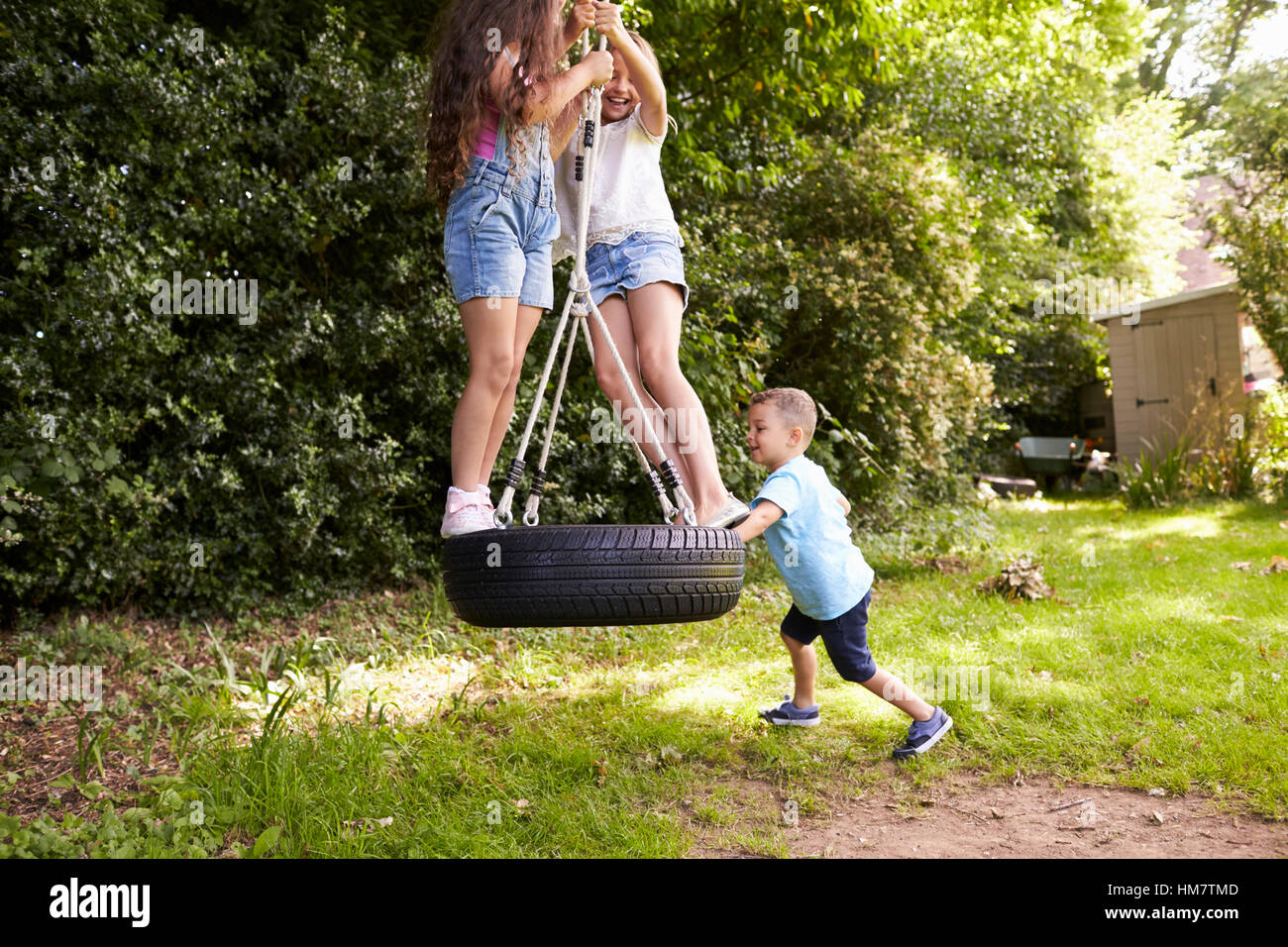 Group Of Children Playing On Tire Swing In Garden Stock Photo