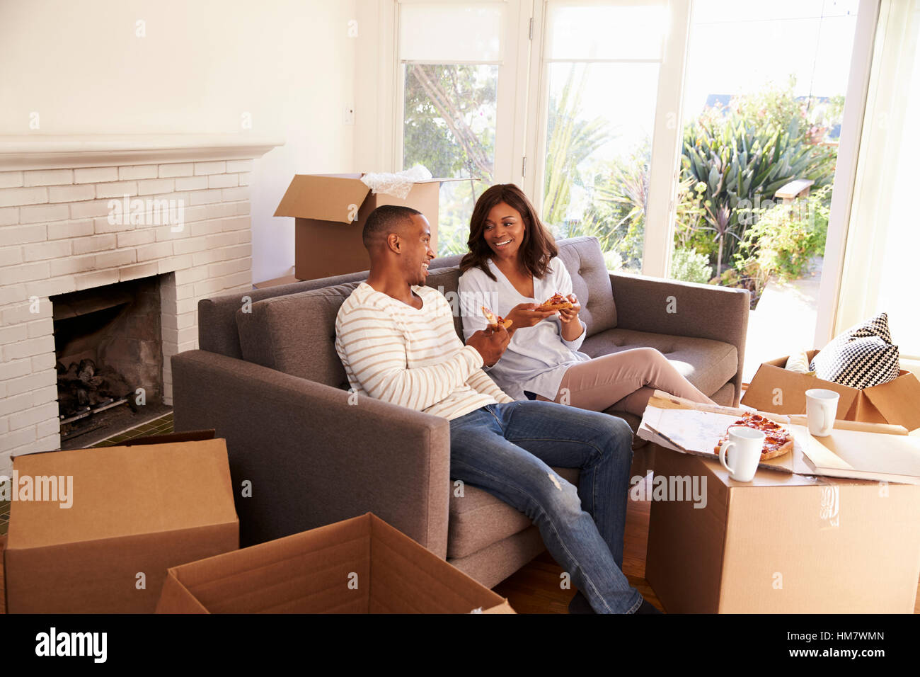 Couple Take A Break On Sofa With Pizza On Moving Day Stock Photo