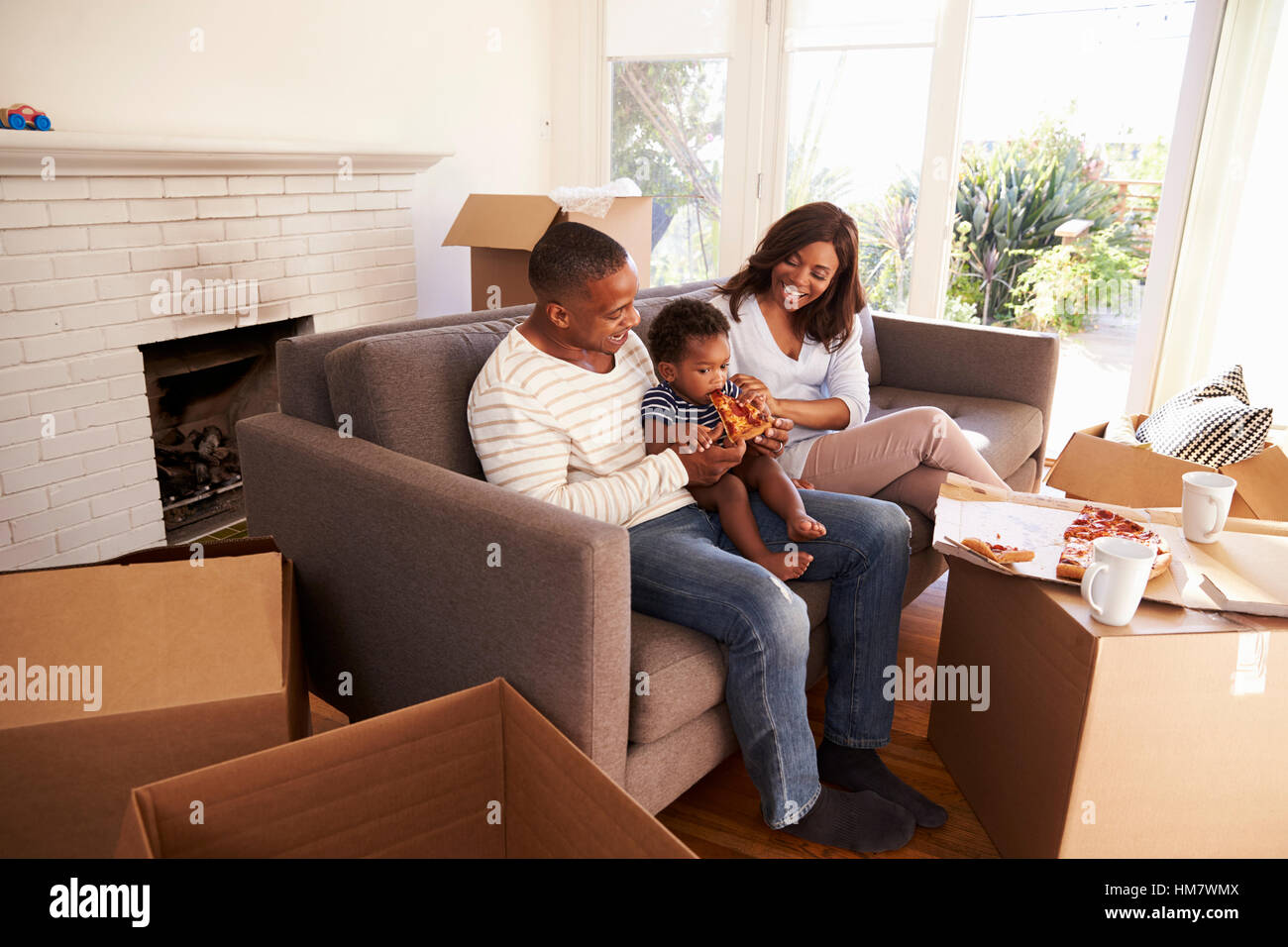 Family Take A Break On Sofa With Pizza On Moving Day Stock Photo