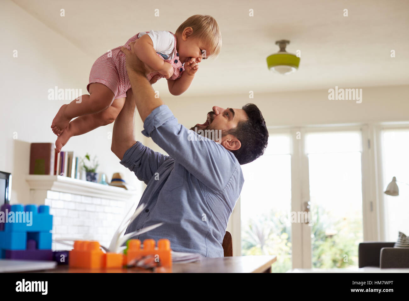 Father Sits At Table And Plays With Baby Son At Home Stock Photo