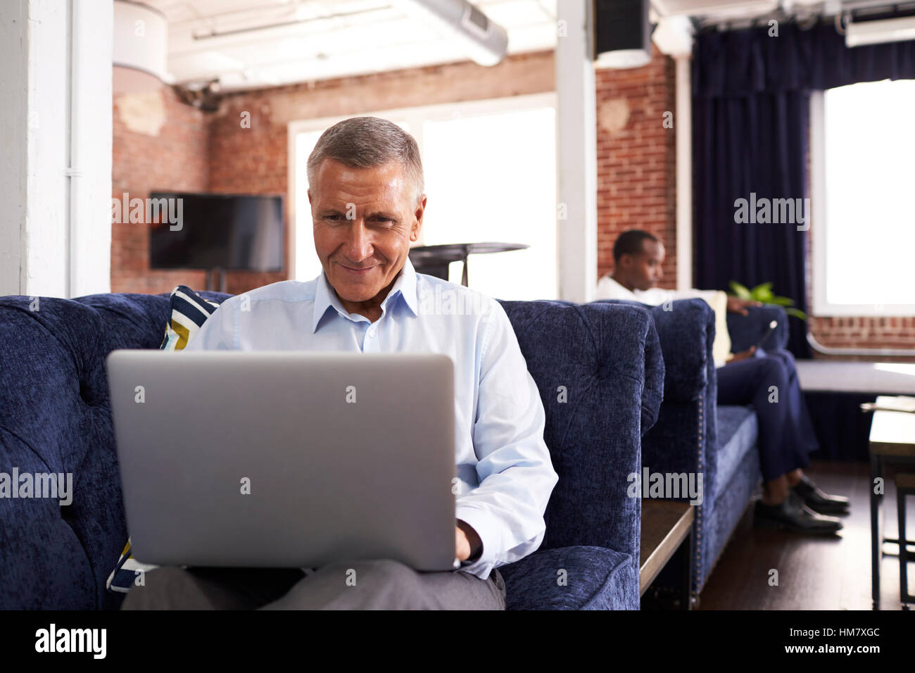 Businessmen Working On Sofas In Relaxation Area Of Office Stock Photo