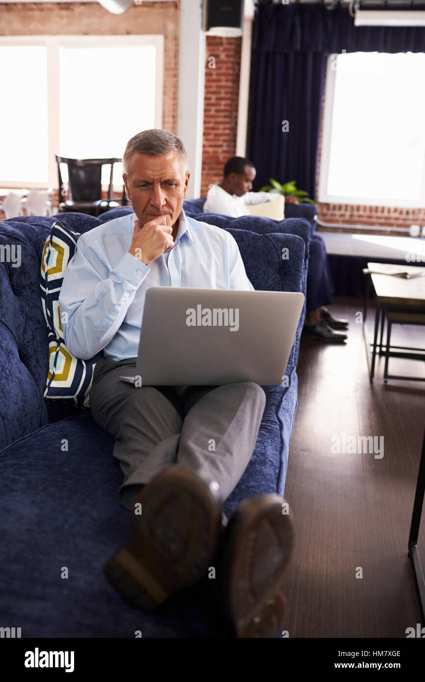 Businessmen Working On Sofas In Relaxation Area Of Office Stock Photo