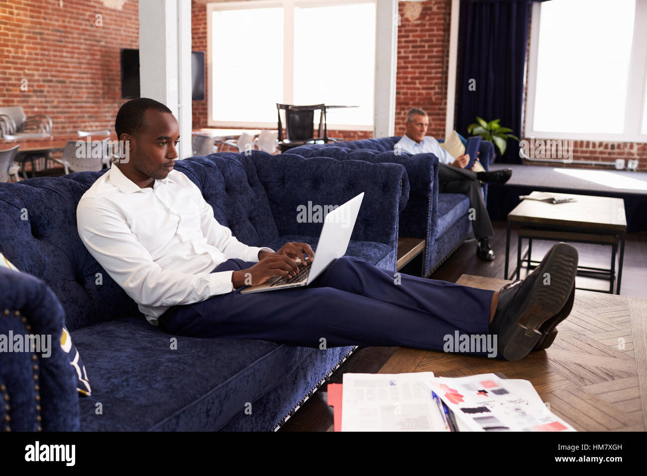 Businessmen Working On Sofas In Relaxation Area Of Office Stock Photo