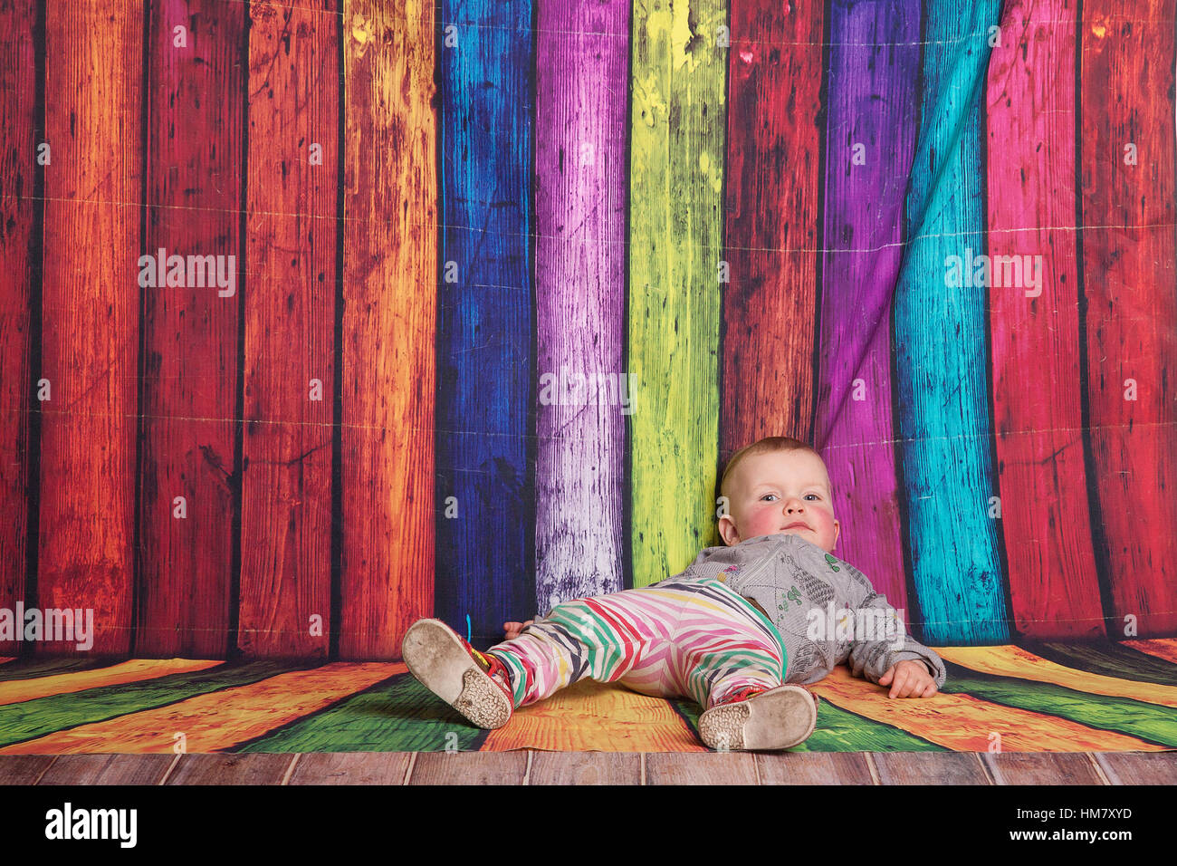 Baby kid in front of color full background lying down bored. Stock Photo