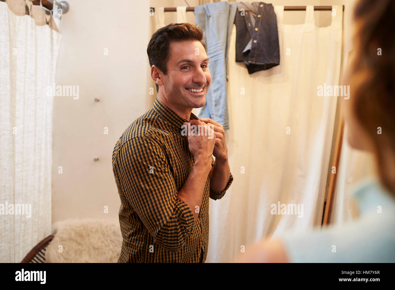 Woman watches her partner trying on shirt in changing room Stock Photo