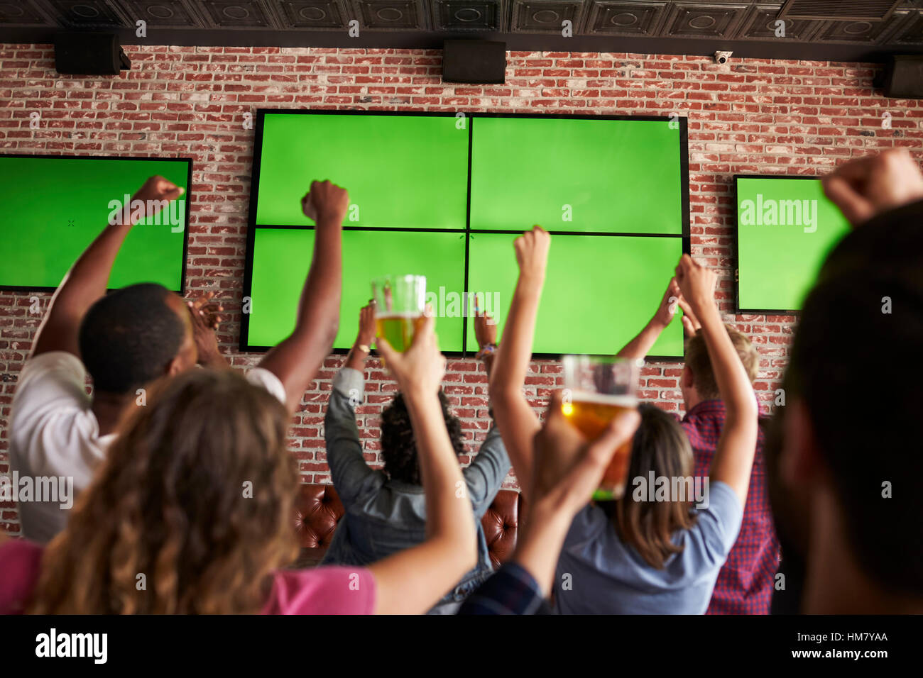 Rear View Of Friends Watching Game In Sports Bar On Screens Stock Photo
