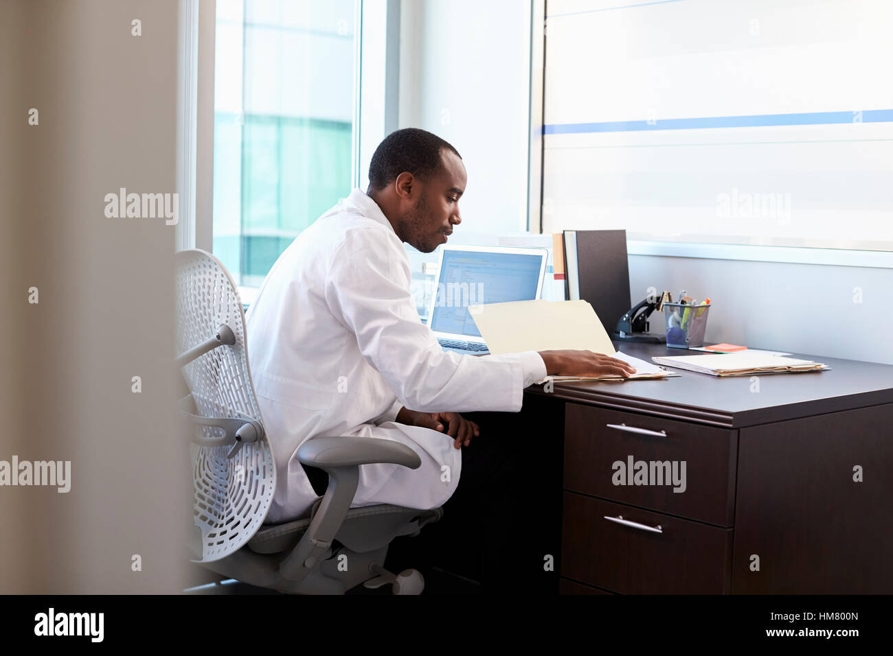 Doctor Wearing White Coat Reading Notes In Office Stock Photo