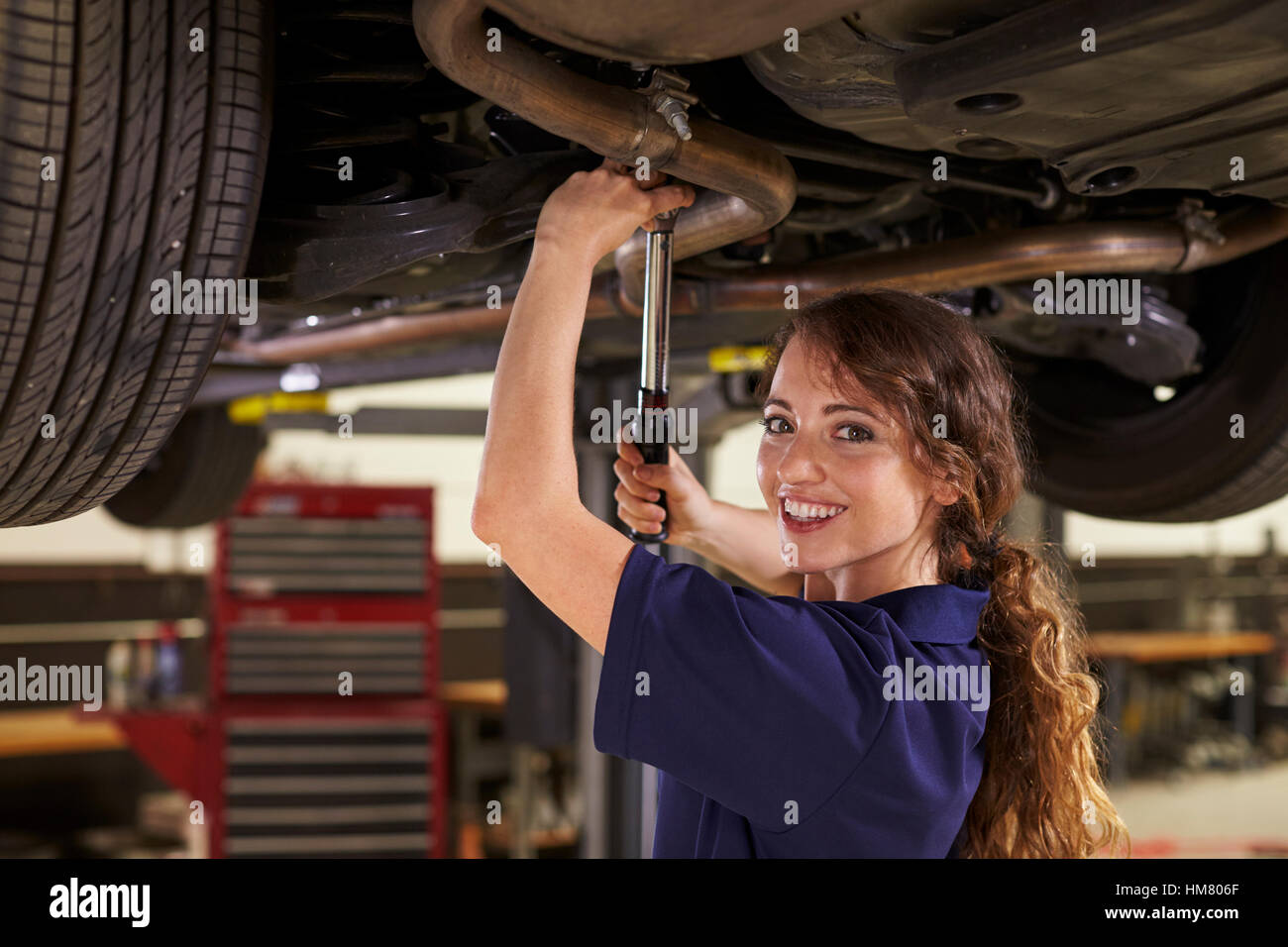Portrait Of Female Auto Mechanic Working Underneath Car Stock Photo